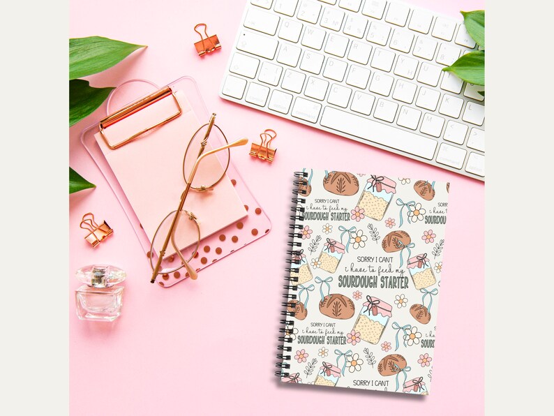 May include: A white spiral bound notebook with a cute illustration of a sourdough starter and bread. The notebook has a repeating pattern of the illustration and the text "Sorry I can't I have to feed my sourdough starter".