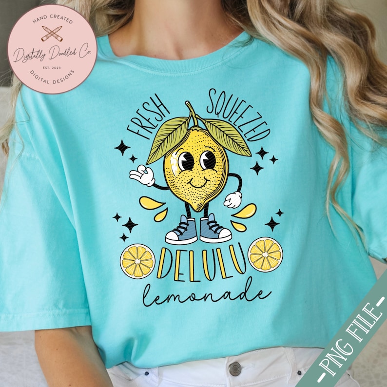 Pu&ograve; includere: Una maglietta turchese con un disegno di limone a cartone animato. Il limone ha un viso sorridente e indossa scarpe da ginnastica. Il testo "FRESH SQUEEZED DELULU lemonade" &egrave; stampato sulla maglietta.