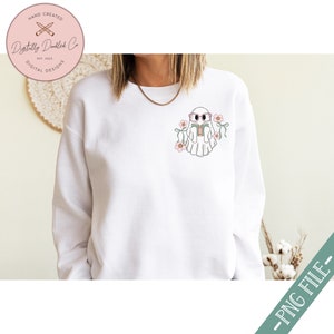 K&ouml;nnte beinhalten: Wei&szlig;er Pullover mit einem niedlichen Geist, der eine Brille tr&auml;gt und ein Buch liest. Der Geist ist von rosa Blumen umgeben. Der Text "Digitally Doodled Co. Est. 2023 Digital Designs" befindet sich in der oberen linken Ecke des Pullovers.