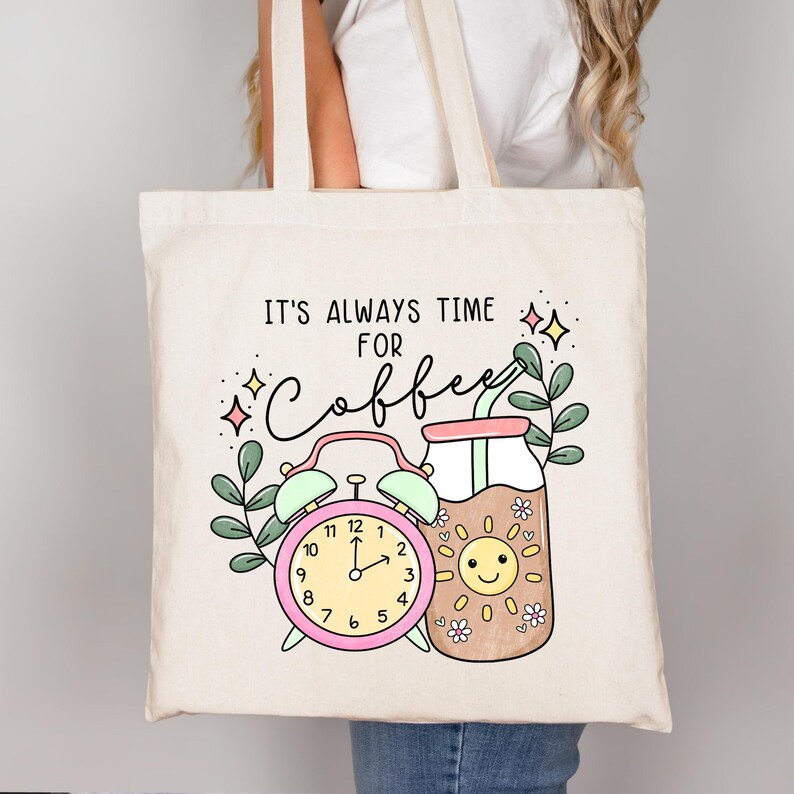 May include: A white canvas tote bag with the text "IT'S ALWAYS TIME FOR COFFEE" in black. The design features a pink alarm clock, a brown glass with a straw, and a yellow sun with a smiling face.
