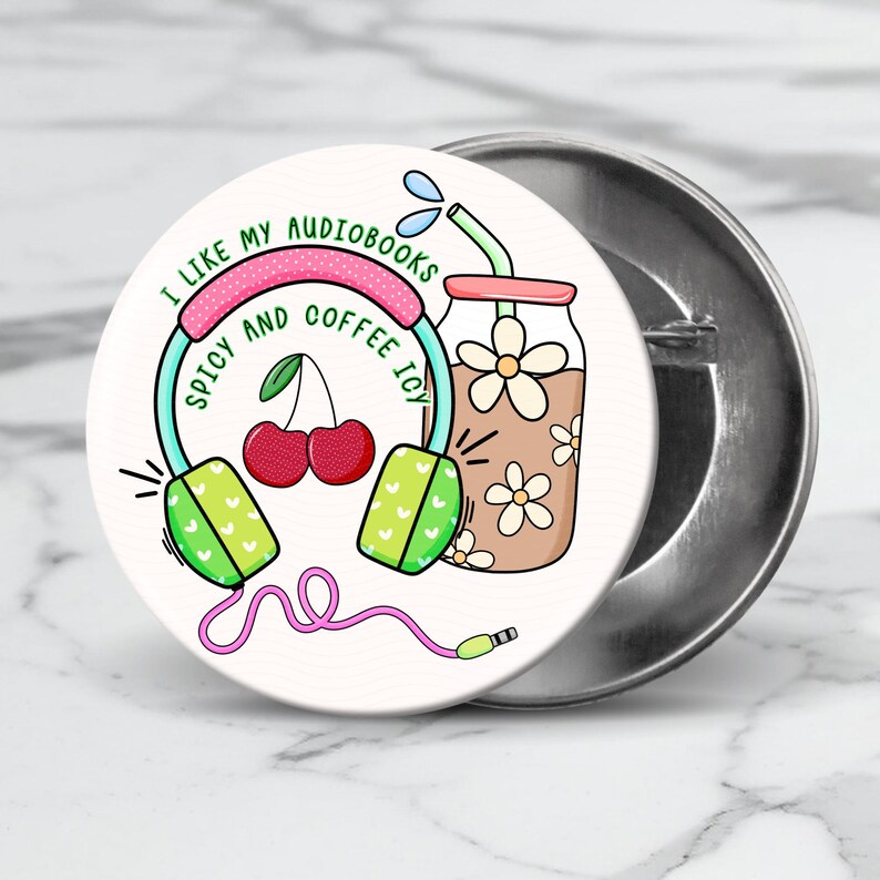 May include: A white button with a pink, green, and blue illustration of headphones, a glass of iced coffee, and cherries. The text on the button reads "I like my audiobooks spicy and coffee icy."
