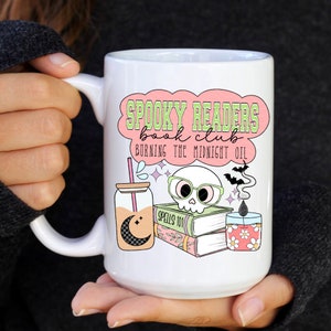 May include: White ceramic mug with a pink and green design that says "Spooky Readers Book Club Burning the Midnight Oil". The design also includes a skull wearing glasses, a book stack, a jar with a straw, and a candle.