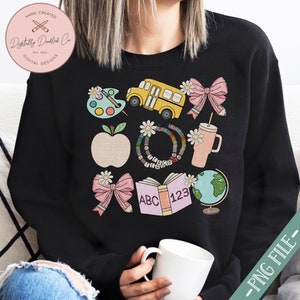 May include: Black sweatshirt with a colorful school-themed graphic. The design includes a yellow school bus, apple, books, globe, and bows. The text "HAND CREATED" and "Digitally Dindled Co" are visible. The words "ABC" and "123" are on a book.