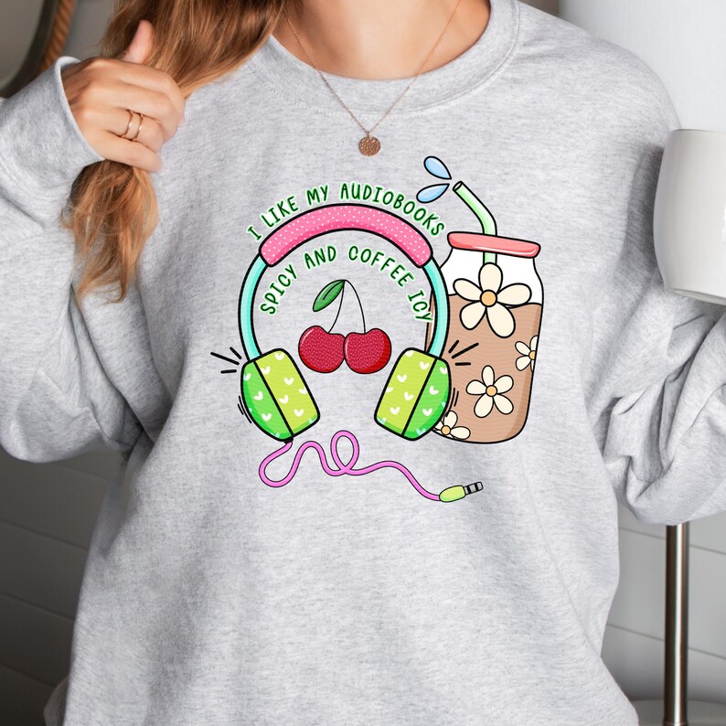 May include: Gray sweatshirt with a graphic design featuring headphones, cherries, and a glass of iced coffee. The text reads "I like my audiobooks spicy and coffee icy."
