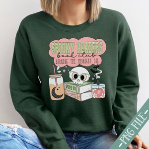 May include: A dark green sweatshirt with a pink and white graphic design that says "Spooky Readers Book Club Burning the Midnight Oil". The graphic also includes a skull with glasses, a book, a candle, and a glass of liquid.