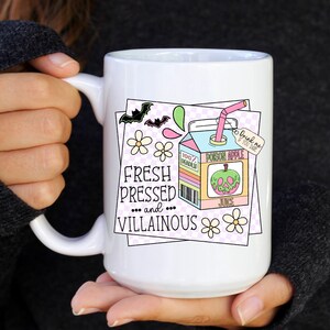 May include: White ceramic mug with a colorful illustration of a cartoon poison apple juice box with the text "Fresh Pressed... and... Villainous" and a bat, flowers, and a checkered background.