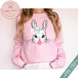 May include: A pink sweatshirt with a white bunny wearing a blue and pink bow and blowing a pink bubble. The bunny has black eyes and a black nose.
