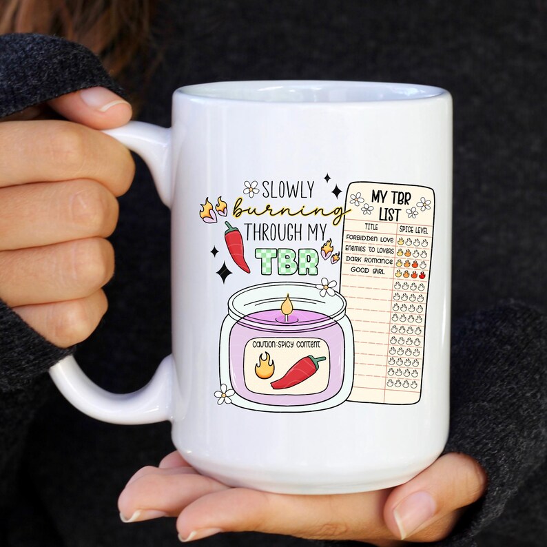 May include: White ceramic mug with a graphic of a candle with the text "Slowly burning through my TBR" and a list of book titles with a spice level rating.