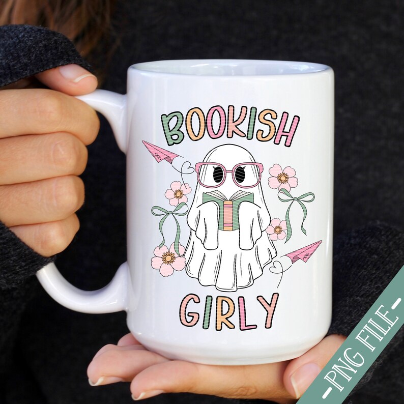 K&ouml;nnte beinhalten: Eine wei&szlig;e Keramiktasse mit einem Geist, der eine rosa Brille tr&auml;gt und ein Buch liest. Der Geist ist von rosa Blumen und Papierflugzeugen umgeben. Der Text "BOOKISH GIRLY" ist auf die Tasse gedruckt.