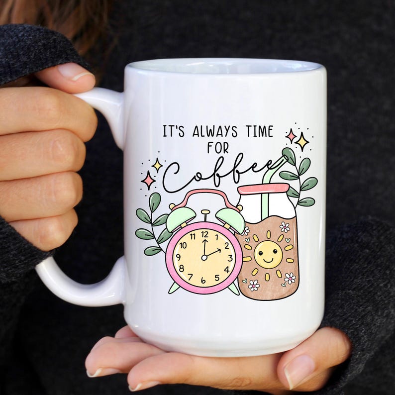 May include: White ceramic mug with a pink alarm clock and a glass of coffee with a sun face. The mug has the text "It's always time for coffee" in black.
