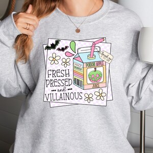 May include: A gray sweatshirt with a graphic design of a cartoon juice box with a skull-shaped apple and the text "Fresh Pressed... and... Villainous" and "Poison Apple Juice" and "Drink me if you dare".