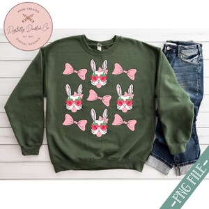 May include: Green sweatshirt with a white bunny wearing pink bows and strawberry sunglasses. The bunny is repeated multiple times on the sweatshirt.