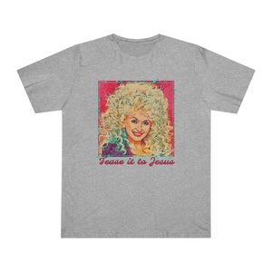 Puede incluir: Camiseta gris con un retrato de una mujer con cabello rubio rizado. El retrato está enmarcado en un rectángulo rosa con detalles turquesa y el texto "Tease it to Jesus" en escritura rosa.