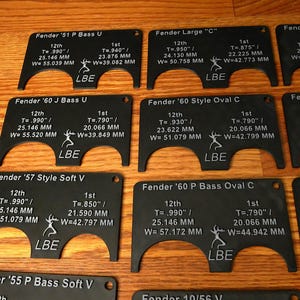 May include: A set of ten black plastic guitar nut measuring templates. Each template is labeled with the guitar model, the string position, and the measurement in inches and millimeters. The templates are arranged in two rows of five.