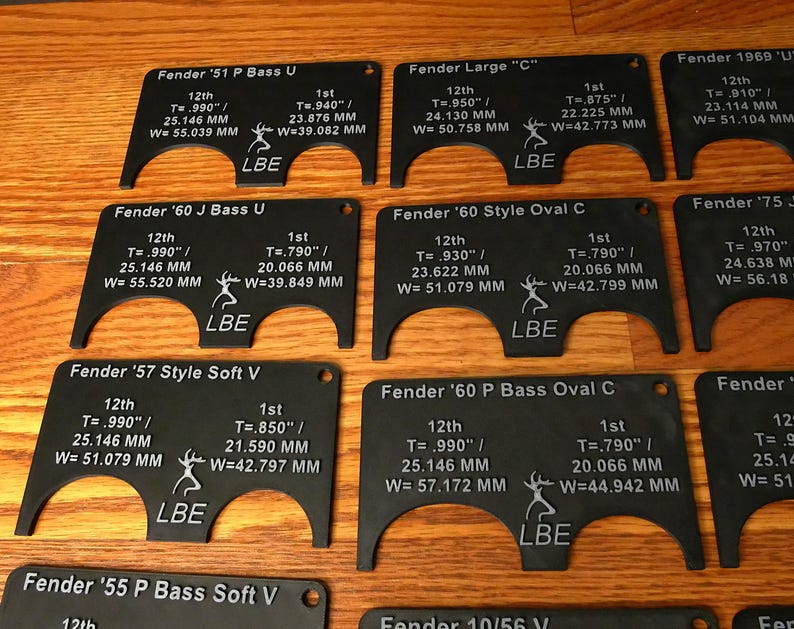 May include: A set of ten black plastic guitar nut measuring templates. Each template is labeled with the guitar model, the string position, and the measurement in inches and millimeters. The templates are arranged in two rows of five.
