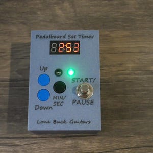 May include: A blue pedalboard set timer with a digital display showing 88:88. The timer has two blue buttons labeled "Up" and "Down", a black button labeled "MIN/SEC", and a silver button labeled "START/PAUSE".