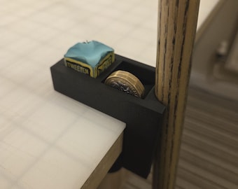 May include: A black 3D-printed pool cue accessory, attached to a table edge. It holds a chalk cube and a coin. The cue is wooden with a light brown and dark brown grain pattern. The chalk is in a blue wrapper with the word "TWEETEN".