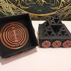 May include: Two black 3D-printed objects with copper-colored circular coil accents. One object is a square box with a circular labyrinth pattern on top labeled MWO EMFS. The other is a pyramid with a fractal Sierpinski triangle design.
