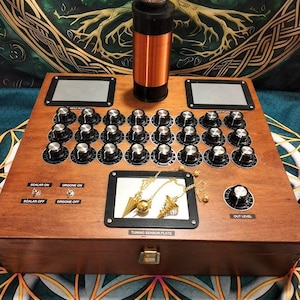 Puede incluir: Una caja de madera con un panel de control con numerosas perillas, interruptores y una placa de sensor de afinación. Una bobina de cobre y una esfera plateada están en la parte superior. El texto "SCALAR ON", "ORGONE ON", "SCALAR OFF" y "ORGONE OFF" son visibles.
