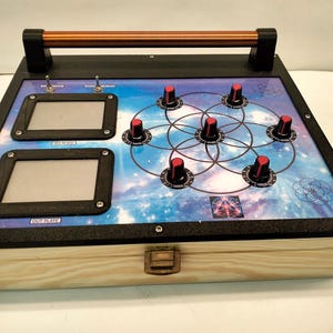Może przedstawiać: Drewniana skrzynka z czarnym blatem z dwoma prostokątnymi ekranami, przełącznikami dźwigniowymi i kilkoma pokrętłami z czerwonymi nakładkami. Blat ma motyw galaktyki z geometrycznym wzorem i miedzianym uchwytem.