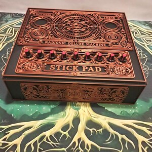 Puede incluir: Una máquina Radionic Deluxe rectangular de color negro con grabados intrincados en color cobre. El panel superior presenta un diseño geométrico central, diales circulares y el texto WITNESS, TREND y STICK PAD. El frente muestra patrones de cobre a juego.