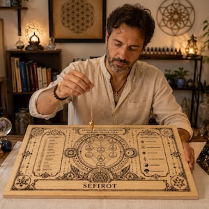 Può includere: Un pannello di legno di Seferot con intricati disegni incisi, raffigurante l'Albero della Vita, viene utilizzato con un pendolo. Il pannello è su un tavolo con cristalli e una lampada di sale illuminata. Il testo "SEFIROT" è visibile.