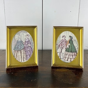 May include: Two framed oval prints of women in 19th century fashion. The prints are in gold frames and feature women in elaborate dresses and hats.