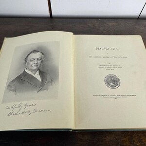 Puede incluir: Un retrato en blanco y negro de un hombre con bigote y barba. El hombre lleva un traje oscuro y una camisa blanca. La imagen es de un libro titulado "Psycho Vox: The Emerson System of Voice Culture" de Charles Wesley Emerson. El libro est&aacute; publicado por el Departamento de Publicaciones del Emerson College of Oratory.
