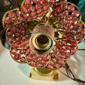 K&ouml;nnte beinhalten: Eine Vintage-Tischlampe mit Messingfu&szlig; und einem pinkfarbenen Kristallblumenmuster. Die Lampe hat eine einzelne Gl&uuml;hbirne und einen wei&szlig;en Marmorsockel.