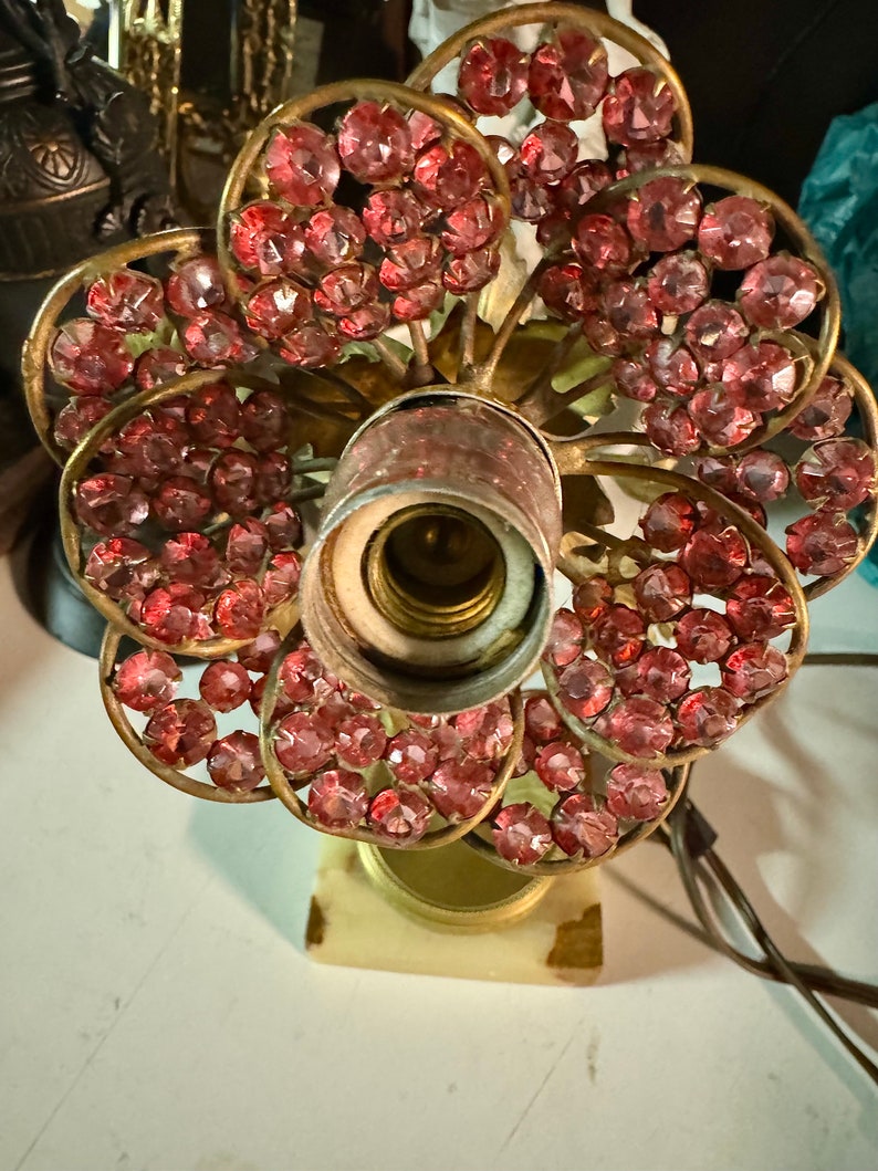 K&ouml;nnte beinhalten: Eine Vintage-Tischlampe mit Messingfu&szlig; und einem pinkfarbenen Kristallblumenmuster. Die Lampe hat eine einzelne Gl&uuml;hbirne und einen wei&szlig;en Marmorsockel.