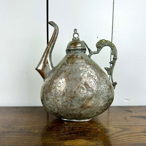 May include: An antique silver teapot with an ornate design and a dragon-shaped handle. The teapot has a round body and a spout that curves upwards.