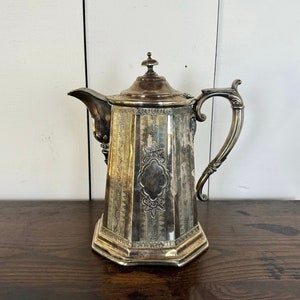 May include: A silver teapot with an ornate design and a octagonal base. The teapot has a lid with a finial and a handle with a scroll design.