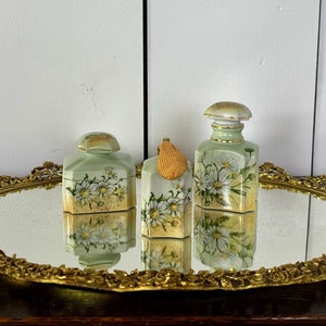 May include: Three vintage porcelain bottles with floral designs and gold accents on a gold-colored tray with a mirrored surface.
