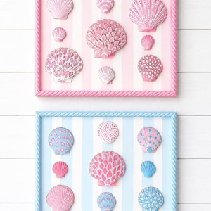 Puede incluir: Dos marcos de pared rectangulares con colecciones de conchas marinas. El marco superior es rosa con rayas blancas y conchas rosas. El marco inferior es azul claro con rayas blancas y una mezcla de conchas rosas y azules. Ambos tienen bordes de cuerda.
