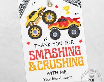 May include: A white gift tag featuring two monster trucks, one yellow and one red, with black tires. The tag includes the text "THANK YOU FOR SMASHING & CRUSHING WITH ME!" and a small trophy graphic. A string is attached at the top.