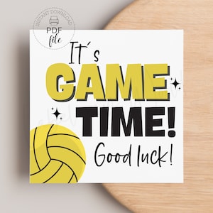 以下が含まれることがあります： 黒と黄色の文字で「It's GAME TIME! Good luck!」と書かれた白いカード。左下の隅に黒のラインが入った黄色のバレーボールがある。