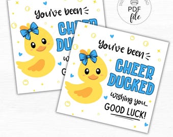 Puede incluir: Dos etiquetas de regalo imprimibles con un pato de goma amarillo con un lazo azul. El texto en las etiquetas dice "You've been Cheer Ducked Wishing you... Good Luck!" Las etiquetas miden 2,5 pulgadas por 2,5 pulgadas.