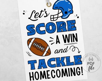 Könnte beinhalten: Weißes Etikett mit blauem Footballhelm und Football-Illustration. Der Text lautet "Let's SCORE A WIN and TACKLE HOMECOMING!" Das Etikett ist mit einer grauen Schnur befestigt und hat eine goldene Öse.