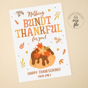 May include: A white Thanksgiving card with the text "Nothing Bundt Thankful for you!" in orange and brown. A cartoon bundt cake with fall leaves and a flower is at the bottom. The words "Happy Thanksgiving!" and "From, Emily" are also included.