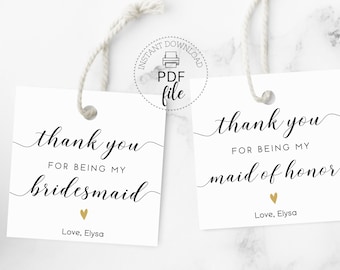 Puede incluir: Dos etiquetas de regalo blancas con caligrafía negra que dice "gracias por ser mi dama de honor" y "gracias por ser mi dama de honor". Ambas etiquetas tienen un pequeño corazón dorado y el texto "Con amor, Elysa".