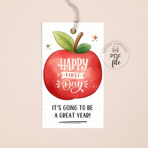 Può includere: Un'etichetta bianca con un'illustrazione di una mela rossa e le parole "HAPPY FIRST DAY". L'etichetta include anche il testo "IT'S GOING TO BE A GREAT YEAR!" e un'icona di file PDF. L'etichetta è attaccata a uno spago beige.