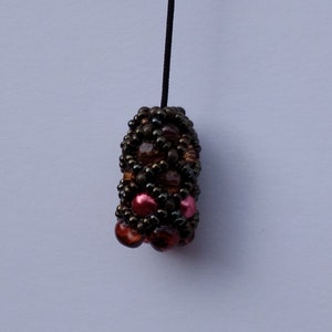 Op de afbeelding: Een kralenhanger met een bruin, zwart en roze kleurenschema. De hanger is gemaakt van kleine, ronde kralen die in een geometrisch patroon zijn gerangschikt.