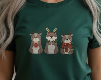 Könnte beinhalten: Dunkelgrünes T-Shirt mit drei Cartoon-Rentieren mit festlichen Accessoires. Die Rentiere tragen ein Herz, einen Kranz und einen Schal. Das T-Shirt hat einen Rundhalsausschnitt.