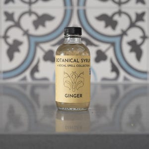Natural ginger syrup bottle with black cap on pastel teal background; label reads Botanical Syrup Ginger