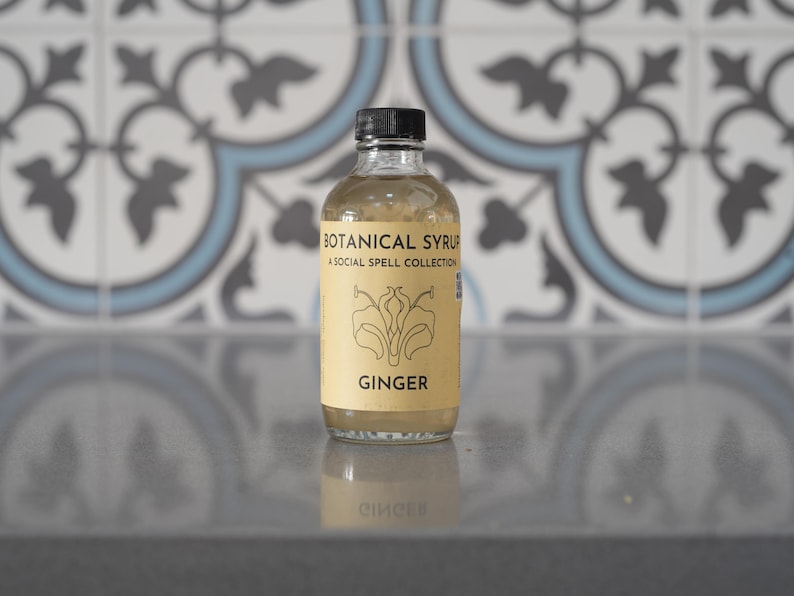 Natural ginger syrup bottle with black cap on pastel teal background; label reads Botanical Syrup Ginger