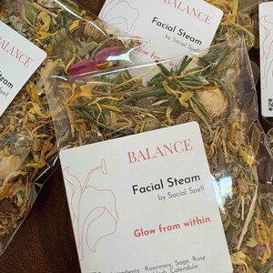 May include: A clear plastic bag filled with dried herbs and flowers for a facial steam. The label reads "BALANCE Facial Steam by Social Spell Glow from within" and lists the ingredients: Rosemary, Sage, Rose petals, Yarrow Herb, Calendula.