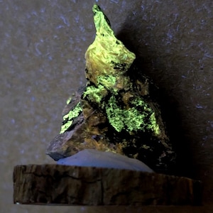 May include: A unique rock formation with a vibrant green glow, possibly due to fluorescence. The rock sits on a rustic, wooden base, creating a striking contrast. The background is a neutral tone, highlighting the rock's unusual color.
