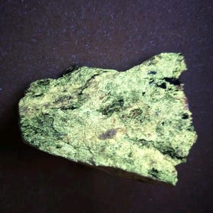 May include: A rough-textured, irregularly shaped rock with a vibrant, glowing green hue. The rock's surface displays a mix of dark and light areas, creating a striking contrast. The overall appearance suggests a mineral specimen or a unique geological find.