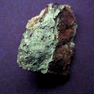 May include: A close-up of a rock with a rough, textured surface. The rock has a light green and brown color palette. The rock is set against a dark purple background.