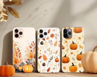 May include: Three smartphone cases featuring autumn-themed designs. The left case displays orange pumpkins and foliage at the base. The center case shows a scattered pattern of leaves and small pumpkins. The right case features a repeating pumpkin print.